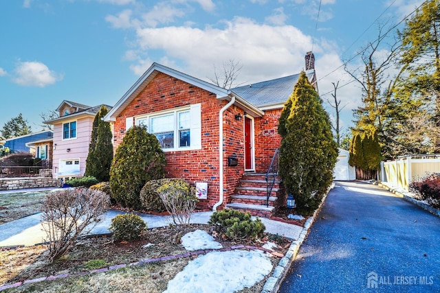 bungalow-style home featuring an outbuilding, fence, brick siding, and a chimney