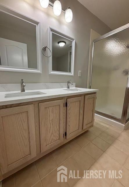 bathroom featuring double vanity, a shower stall, a sink, and tile patterned flooring