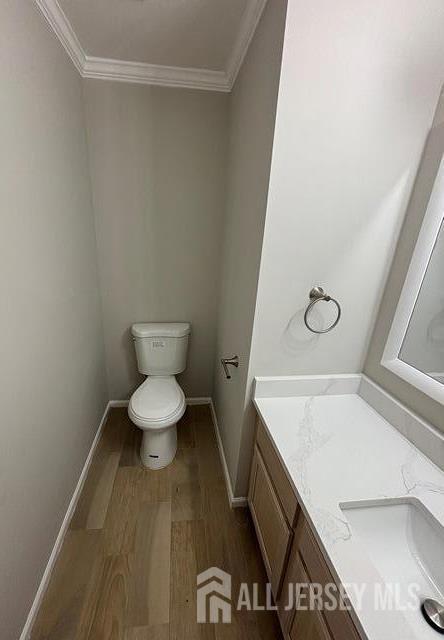 bathroom featuring toilet, ornamental molding, wood finished floors, and vanity