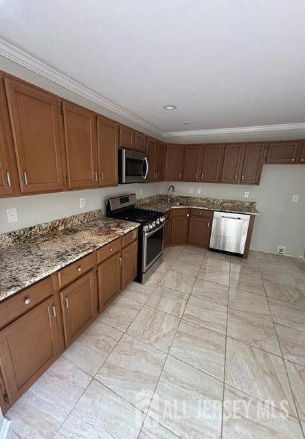 kitchen featuring crown molding, stainless steel appliances, light stone counters, and brown cabinetry