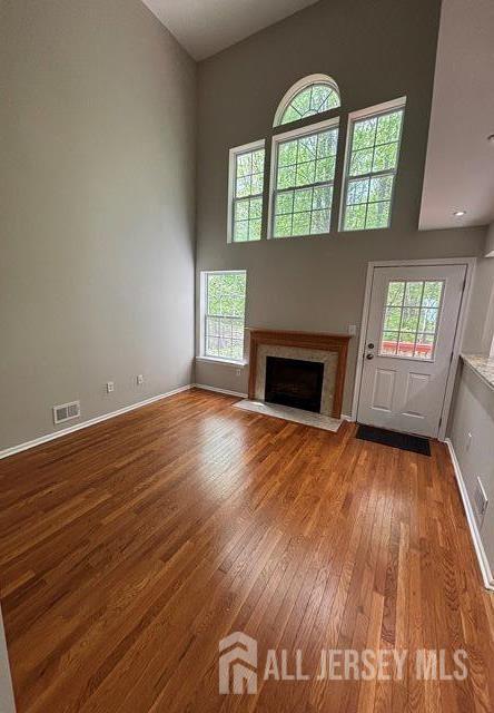 unfurnished living room featuring a high end fireplace, plenty of natural light, hardwood / wood-style flooring, and a towering ceiling