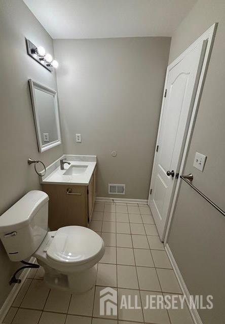 half bath featuring vanity, toilet, tile patterned floors, baseboards, and visible vents