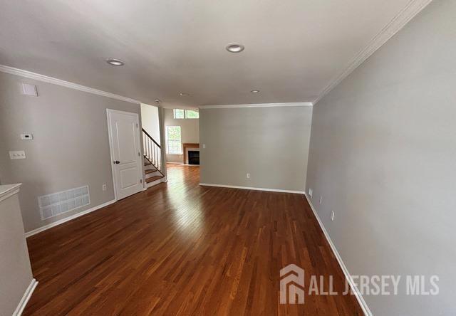 empty room with baseboards, ornamental molding, dark wood finished floors, and visible vents