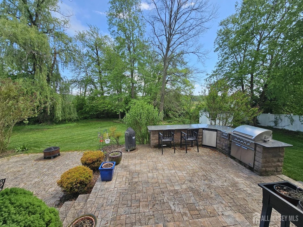 view of patio with fence, outdoor dry bar, a grill, an outdoor fire pit, and an outdoor kitchen