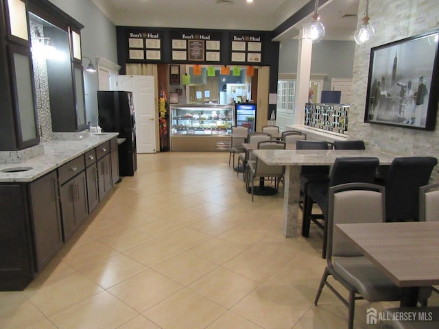 interior space with light tile patterned floors, black refrigerator, hanging light fixtures, a kitchen breakfast bar, and light stone countertops