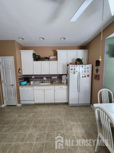 kitchen featuring lofted ceiling with skylight, white cabinetry, sink, decorative backsplash, and white appliances