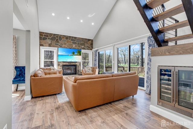 living room with a fireplace, high vaulted ceiling, beverage cooler, light wood-style flooring, and recessed lighting