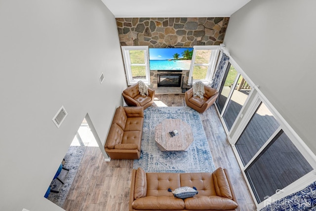 living area featuring wood finished floors, a glass covered fireplace, healthy amount of natural light, and a towering ceiling