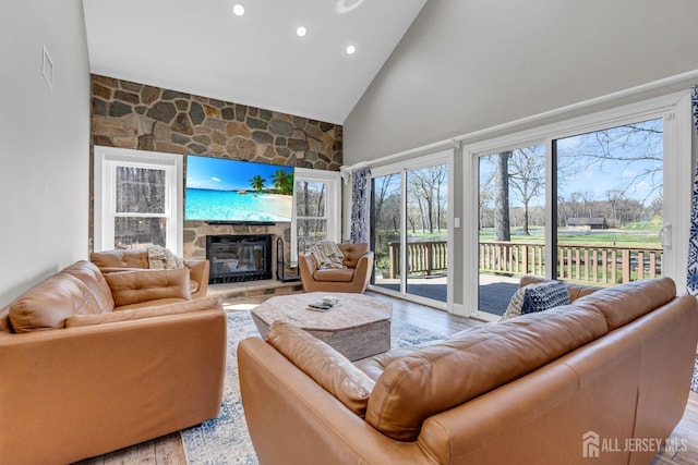 living area with high vaulted ceiling, a stone fireplace, recessed lighting, and wood finished floors