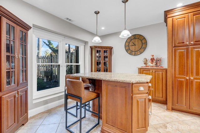 kitchen with a center island, light tile patterned floors, light stone countertops, hanging light fixtures, and glass insert cabinets
