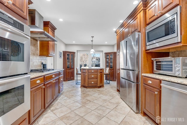 kitchen with appliances with stainless steel finishes, wall chimney range hood, backsplash, brown cabinets, and recessed lighting