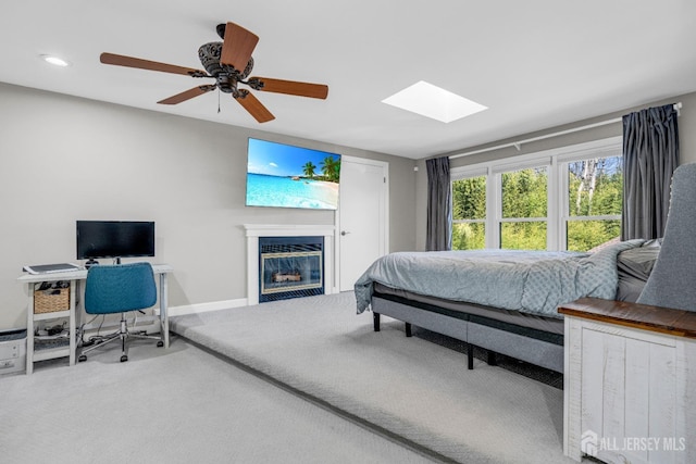 bedroom with carpet floors, a glass covered fireplace, a skylight, baseboards, and recessed lighting