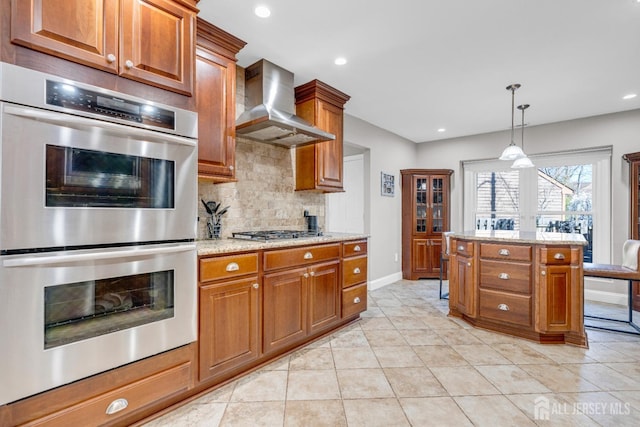 kitchen featuring wall chimney exhaust hood, stainless steel appliances, brown cabinets, backsplash, and light tile patterned flooring