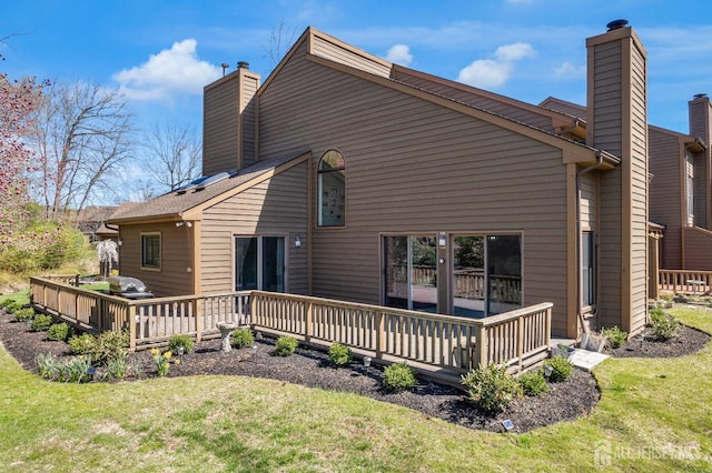 back of house with a chimney, a wooden deck, and a lawn