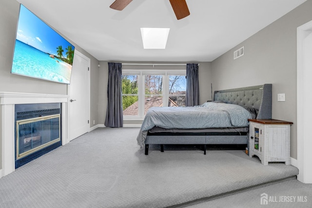 carpeted bedroom with ceiling fan, a glass covered fireplace, baseboards, and a skylight