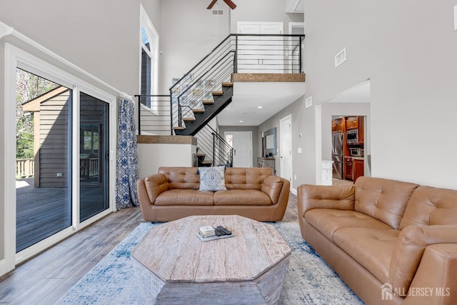 living room featuring stairs, wood finished floors, a high ceiling, baseboards, and a ceiling fan