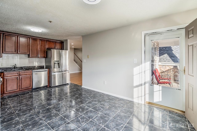kitchen featuring stainless steel appliances, dark countertops, a sink, baseboards, and a textured ceiling