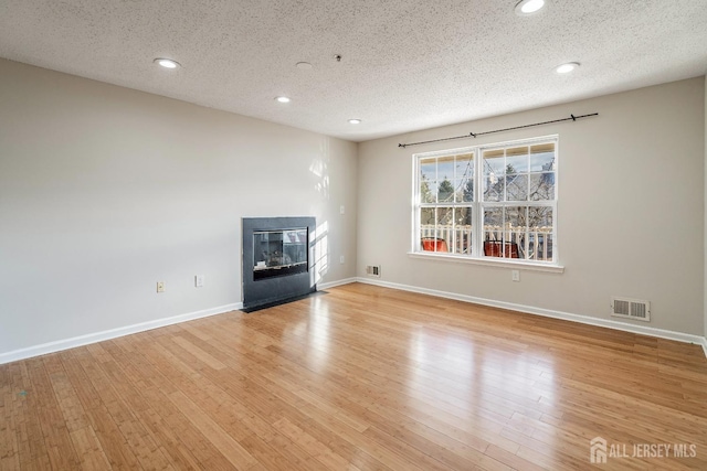 unfurnished living room featuring light wood finished floors, visible vents, baseboards, a fireplace with flush hearth, and a textured ceiling