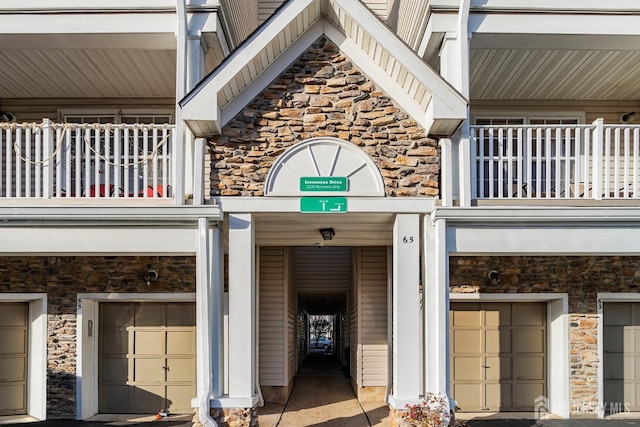 property entrance with stone siding, an attached garage, and a balcony