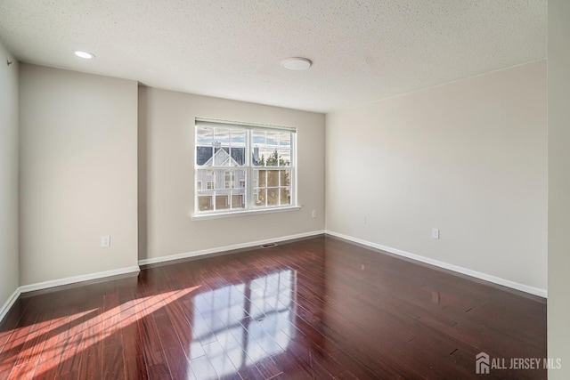 unfurnished room featuring a textured ceiling, dark wood-style floors, and baseboards