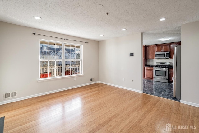 unfurnished living room featuring a textured ceiling, wood finished floors, baseboards, and recessed lighting