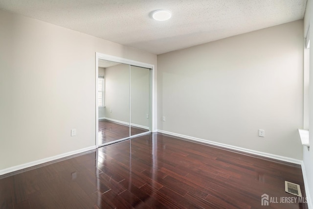 unfurnished bedroom with wood finished floors, visible vents, baseboards, a closet, and a textured ceiling