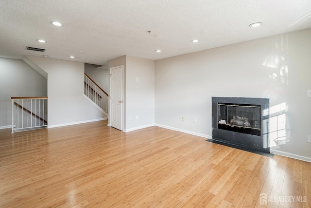 unfurnished living room with wood finished floors, recessed lighting, a textured ceiling, baseboards, and stairway