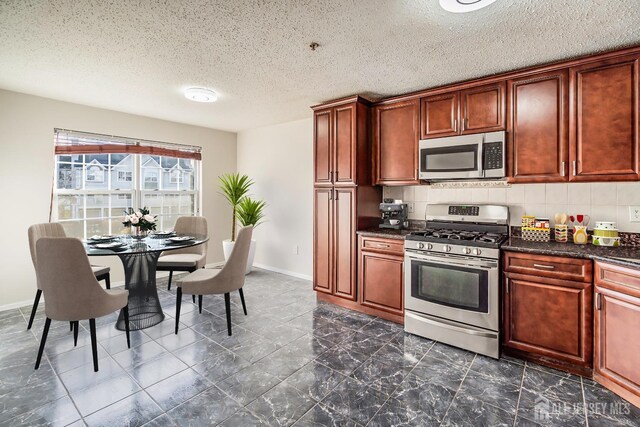 kitchen featuring stainless steel appliances, backsplash, a textured ceiling, baseboards, and dark marble finish floors