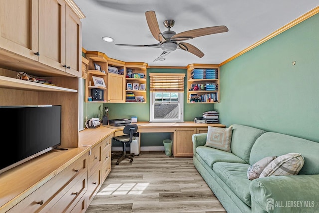 office space with built in desk, light hardwood / wood-style flooring, ceiling fan, and ornamental molding