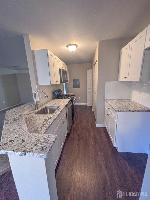 kitchen with appliances with stainless steel finishes, a peninsula, light stone countertops, white cabinetry, and a sink