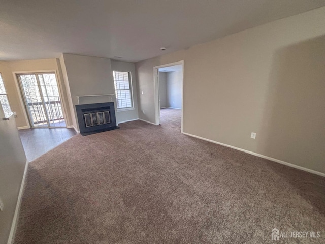 unfurnished living room featuring a fireplace with flush hearth, dark carpet, and baseboards