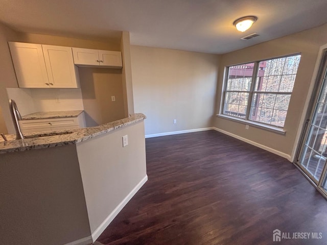 kitchen with visible vents, dark wood finished floors, baseboards, light stone countertops, and white cabinetry