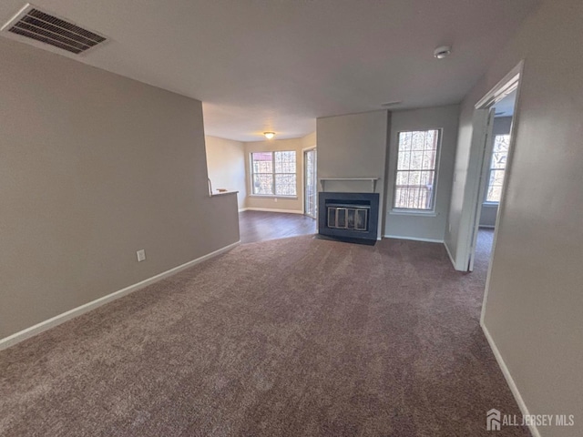 unfurnished living room with dark colored carpet, a fireplace with flush hearth, visible vents, and baseboards