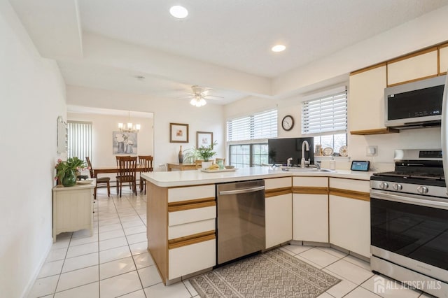kitchen with light countertops, a peninsula, appliances with stainless steel finishes, and ceiling fan with notable chandelier