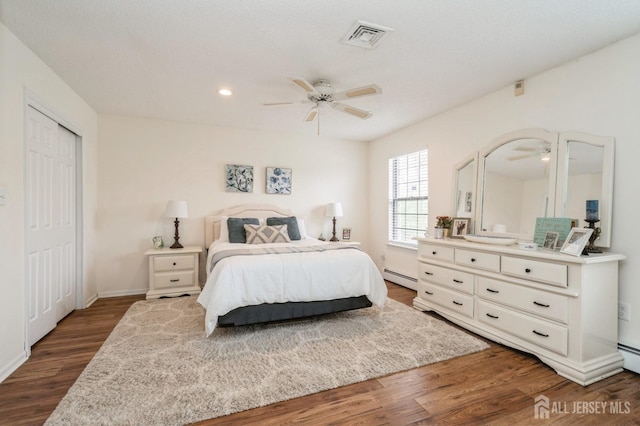 bedroom featuring a ceiling fan, visible vents, dark wood finished floors, baseboards, and a baseboard radiator