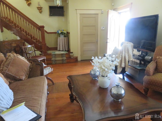 living room featuring stairs, wood finished floors, and an AC wall unit
