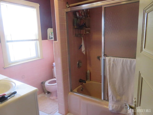 bathroom featuring tile walls, toilet, vanity, and combined bath / shower with glass door