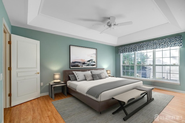 bedroom featuring light wood finished floors, ceiling fan, baseboards, and a tray ceiling