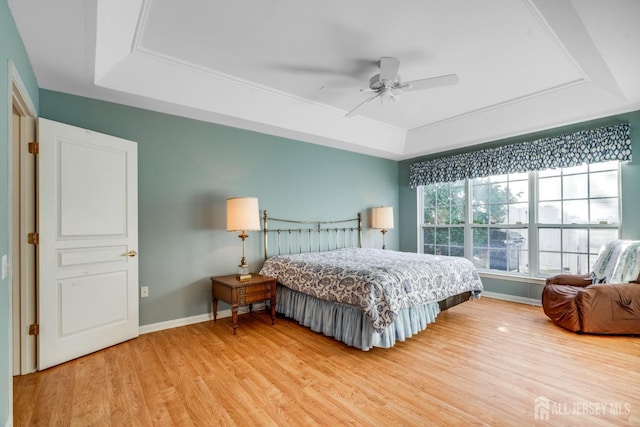 bedroom featuring light wood finished floors, ceiling fan, baseboards, and a tray ceiling