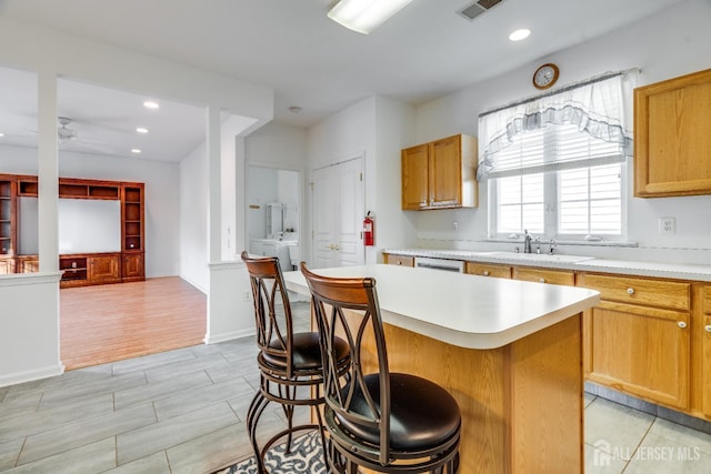 kitchen with recessed lighting, a sink, light countertops, a kitchen bar, and a center island