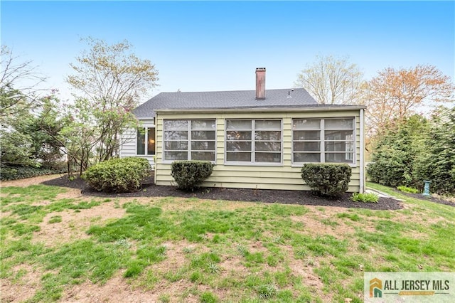 back of house featuring a lawn, a sunroom, and a chimney