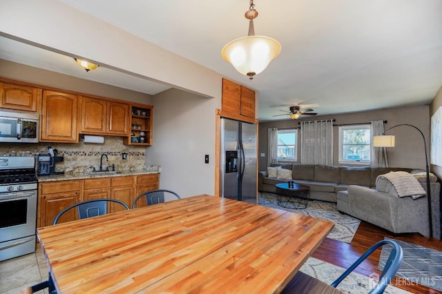 kitchen featuring decorative backsplash, appliances with stainless steel finishes, brown cabinets, pendant lighting, and a sink