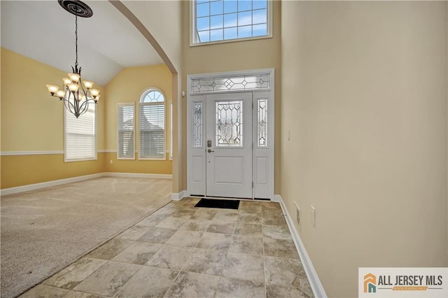 entrance foyer featuring baseboards, lofted ceiling, light carpet, an inviting chandelier, and arched walkways