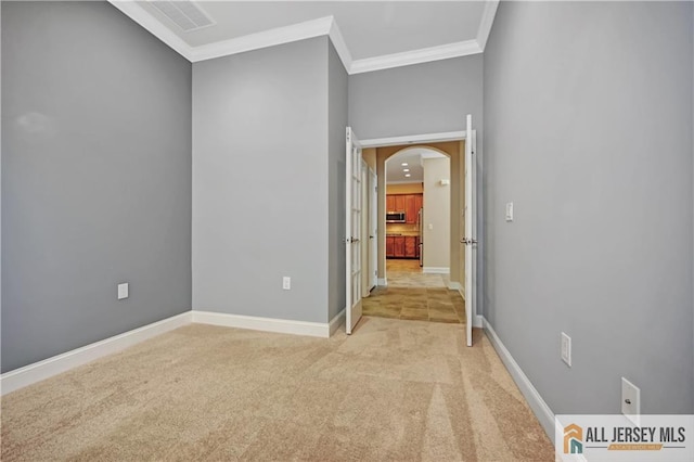 spare room featuring crown molding, baseboards, arched walkways, and light carpet