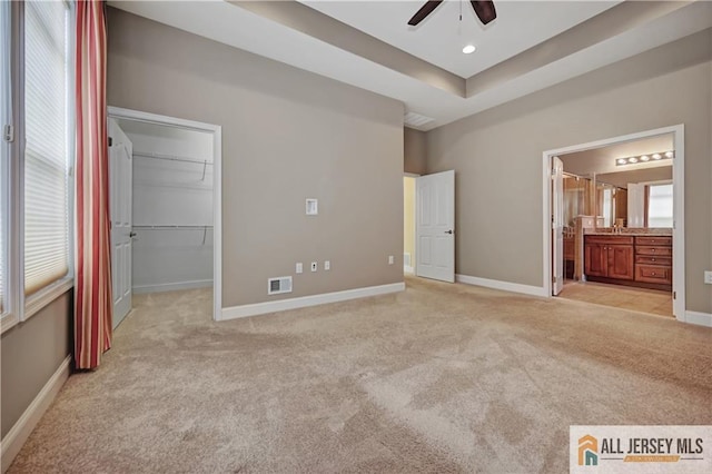 unfurnished bedroom featuring visible vents, a walk in closet, a raised ceiling, baseboards, and light colored carpet