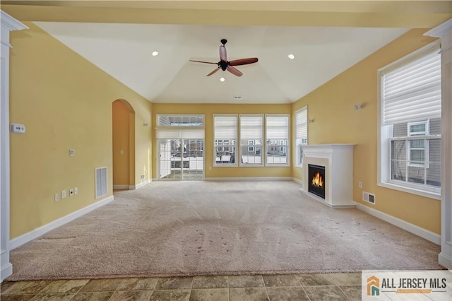 unfurnished living room featuring carpet floors, arched walkways, a lit fireplace, ceiling fan, and vaulted ceiling