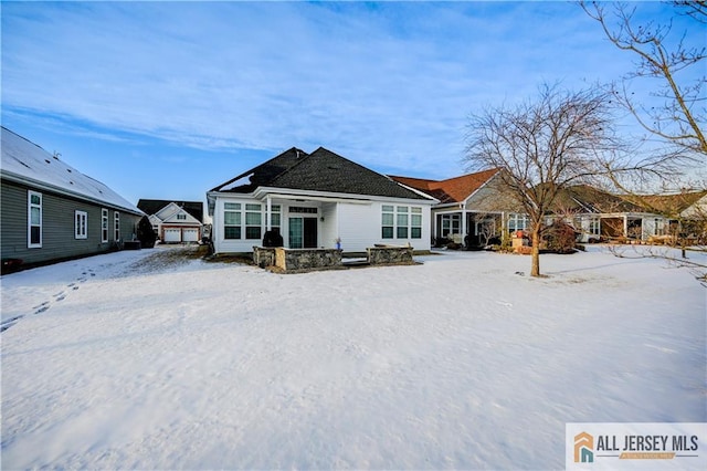 snow covered rear of property featuring a garage and covered porch