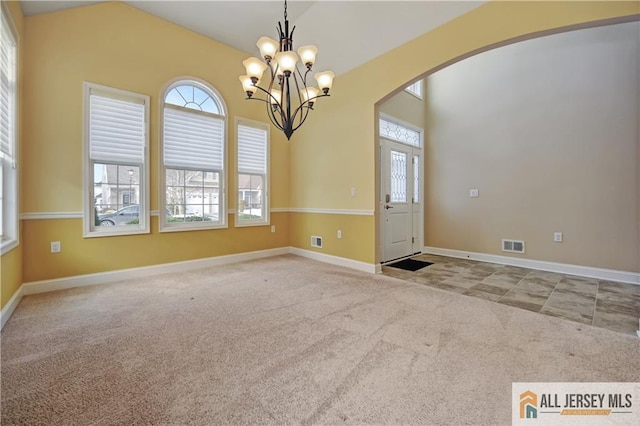 carpeted empty room featuring visible vents, baseboards, lofted ceiling, arched walkways, and a notable chandelier