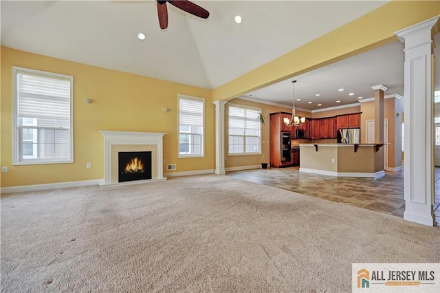 unfurnished living room featuring ornate columns, a warm lit fireplace, crown molding, ceiling fan with notable chandelier, and light colored carpet