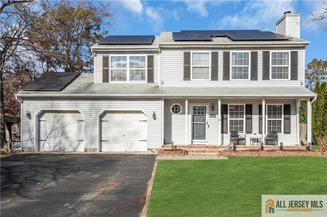 view of front of property with a front yard, solar panels, a garage, and covered porch